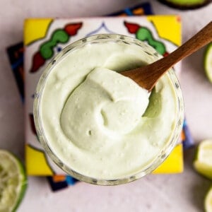 Overhead view of a cup filled with light green colored avocado crema being scooped up with a wooden spoon.