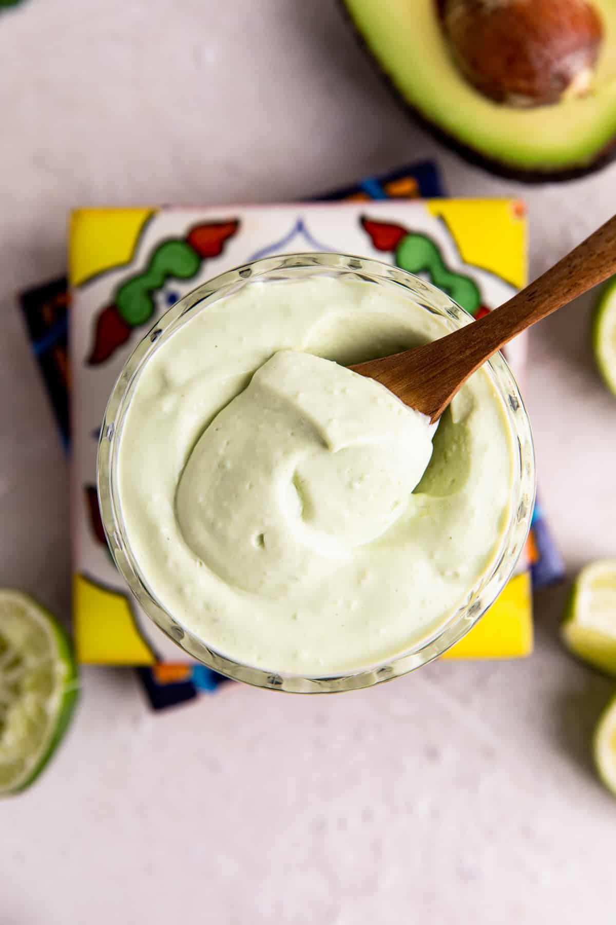 Overhead view of a cup filled with light green colored avocado crema being scooped up with a wooden spoon.