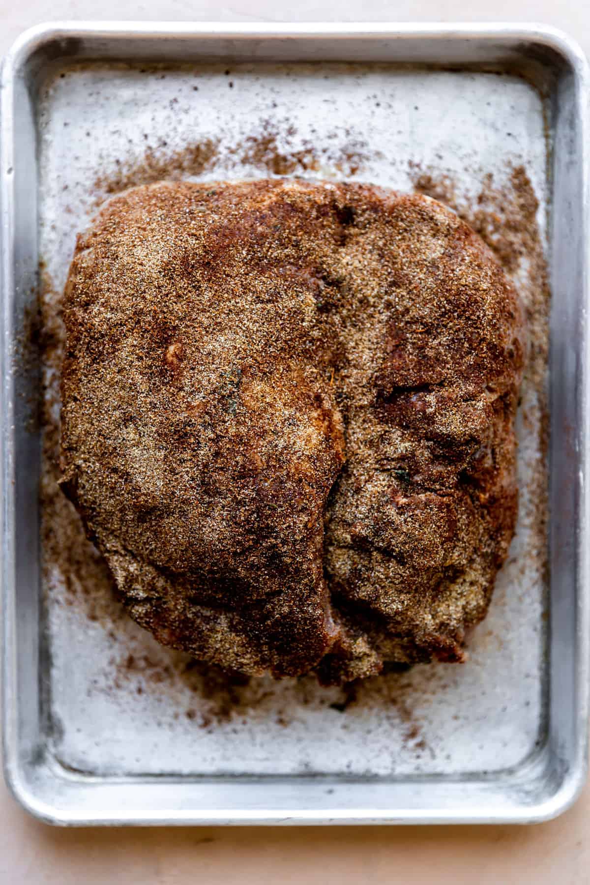 Pork shoulder on a baking sheet and covered with carnitas seasoning blend.