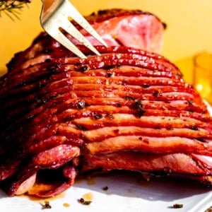 Ham coated with a spicy honey glaze on a white serving plate with a fork separating the slices.