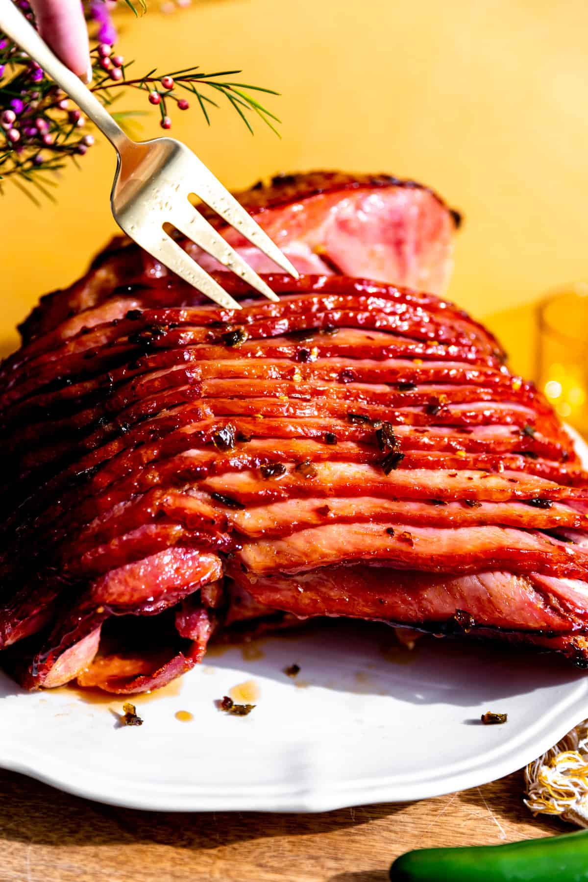 Ham coated with a spicy honey glaze on a white serving plate with a fork separating the slices.