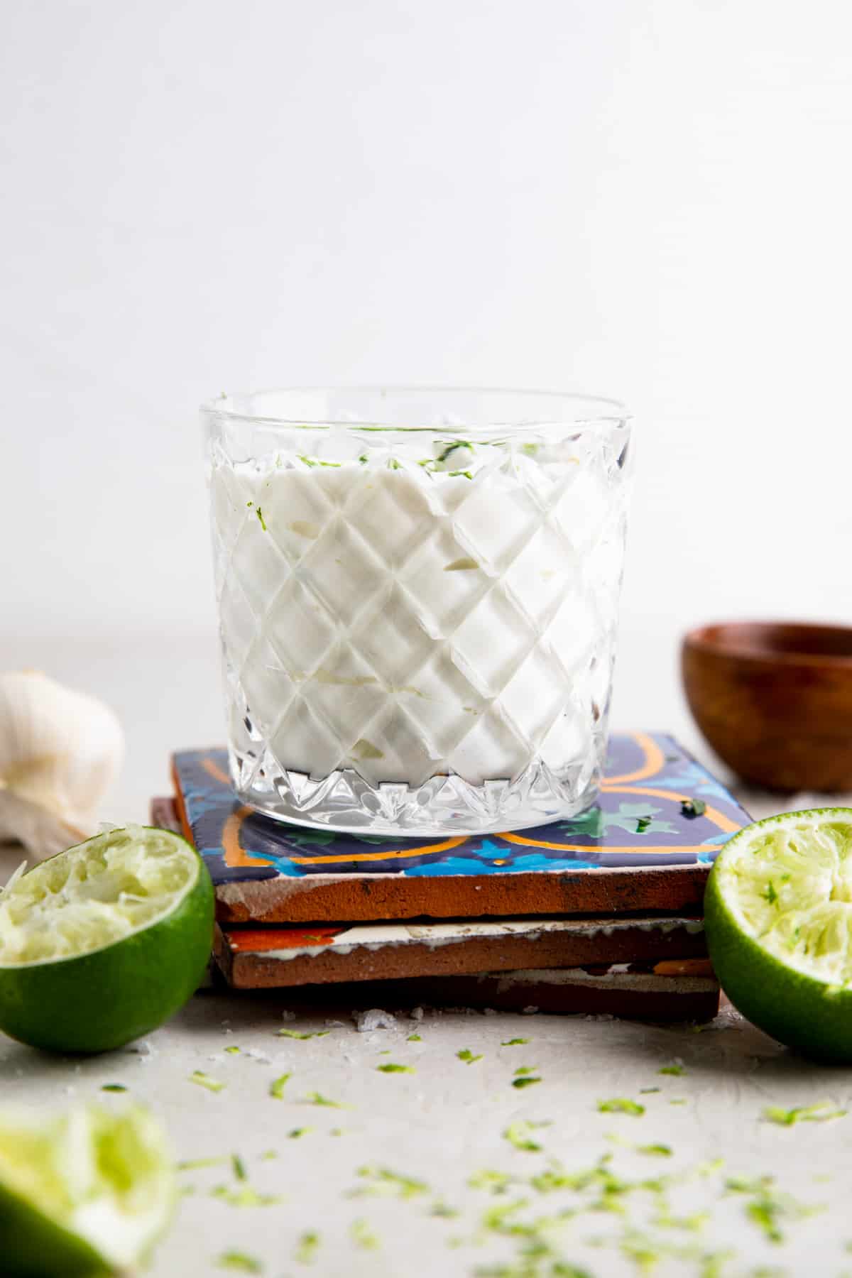 Glass of Lime Crema on a stack of mexican tiles with limes around it.
