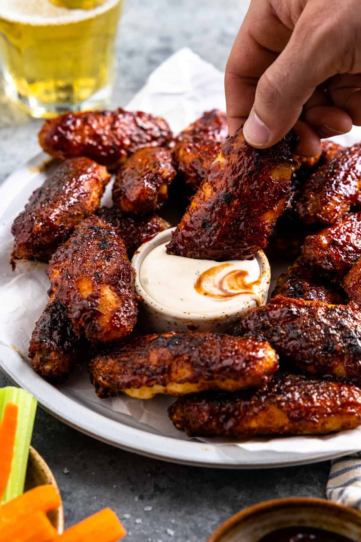 Hand holding a chicken wing with bbq sauce glaze being dipped into a bowl of ranch dressing.