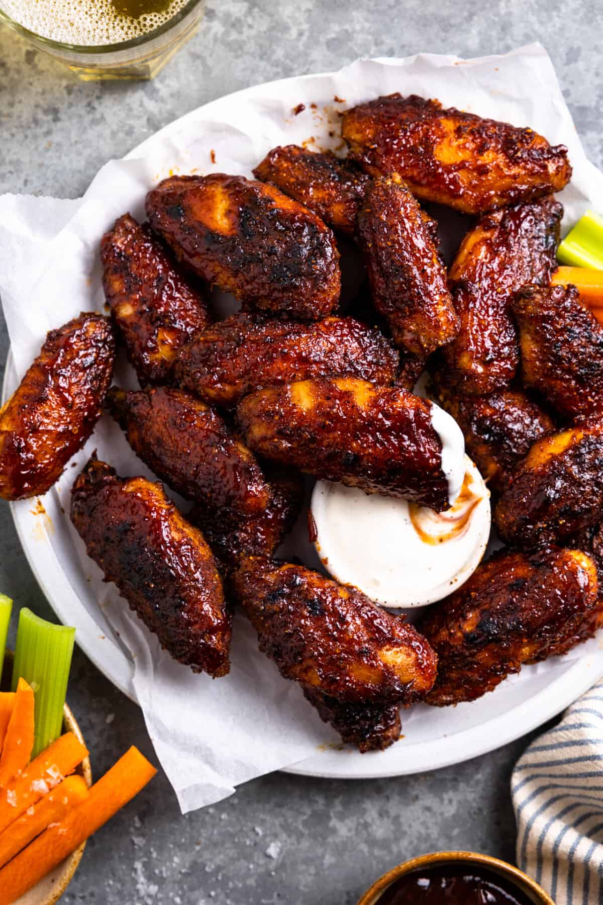 A plate of smoked chicken wings served with a small bowl of ranch, one wing dipped into the ranch.