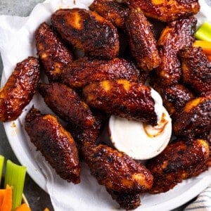 A plate of smoked chicken wings served with a small bowl of ranch, one wing dipped into the ranch.