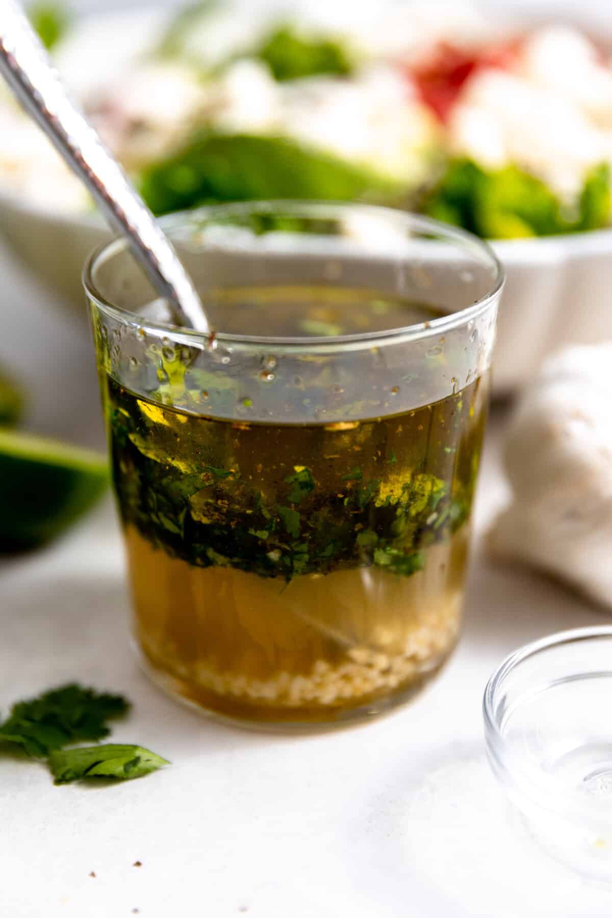 Cup of honey lime vinaigrette with a spoon in it. 