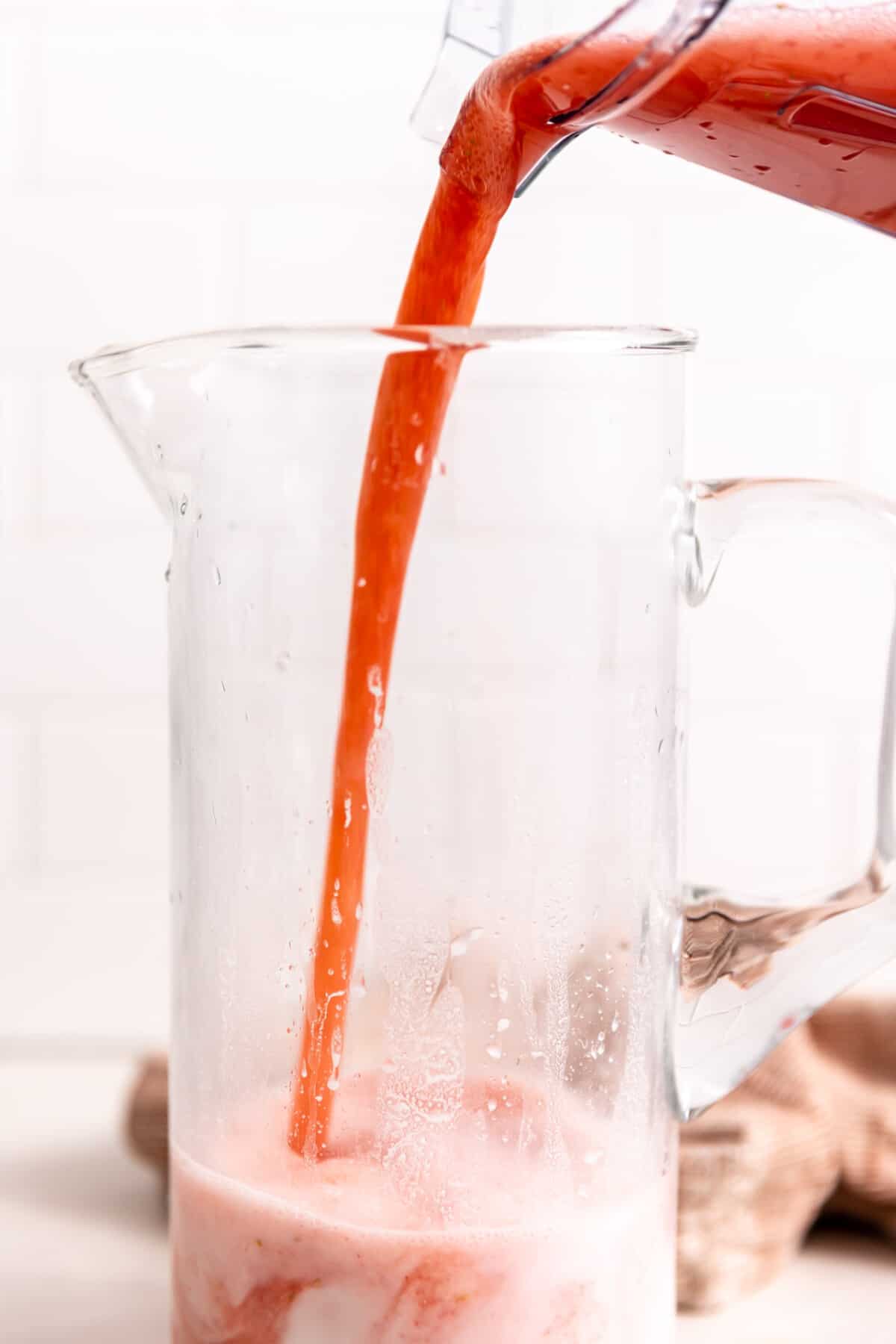 Strawberry juice from blended strawberries being poured into a pitcher with rice milk. 