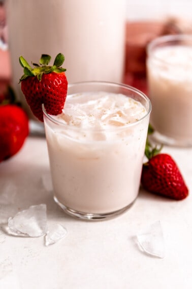 Small glass filled with light pink, strawberry horchata, with a strawberry on the rim of the glass as a garnish.