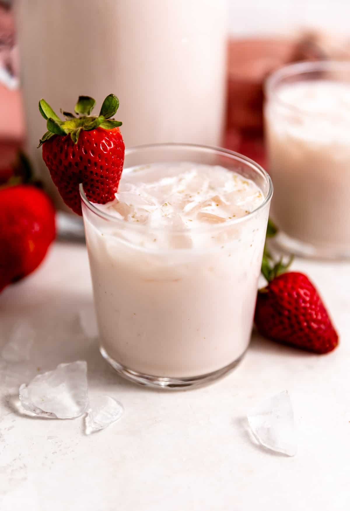 Small glass filled with light pink, strawberry horchata, with a strawberry on the rim of the glass as a garnish.