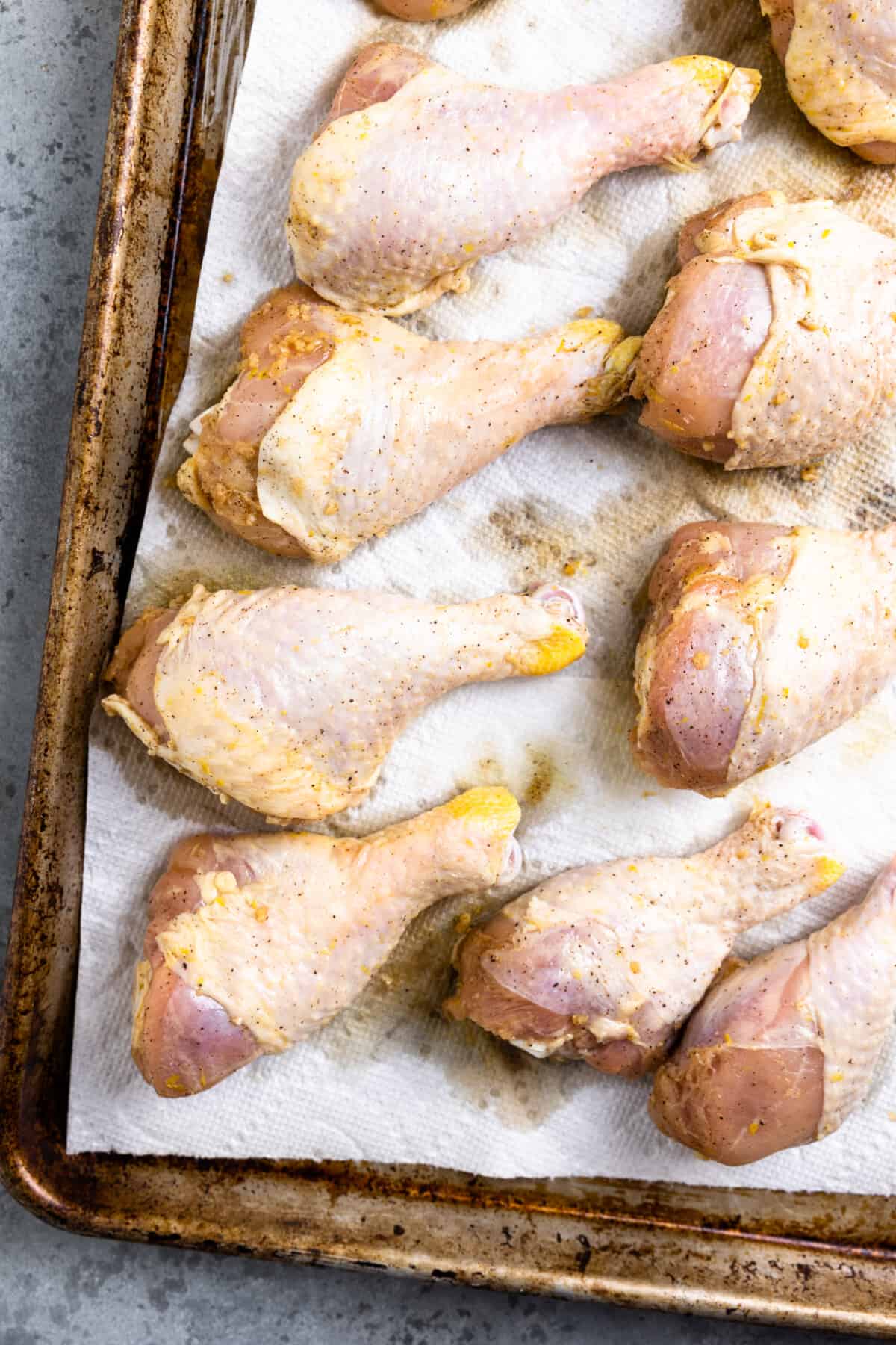 Raw chicken drumsticks on a large baking sheet lined with parchment paper.