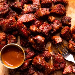Smoked chunks of beef served with a cup of bbq sauce on a piece of brown parchment paper.