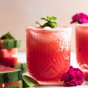 Glass with watermelon margarita garnished with a sprig of mint and salt on the rim.