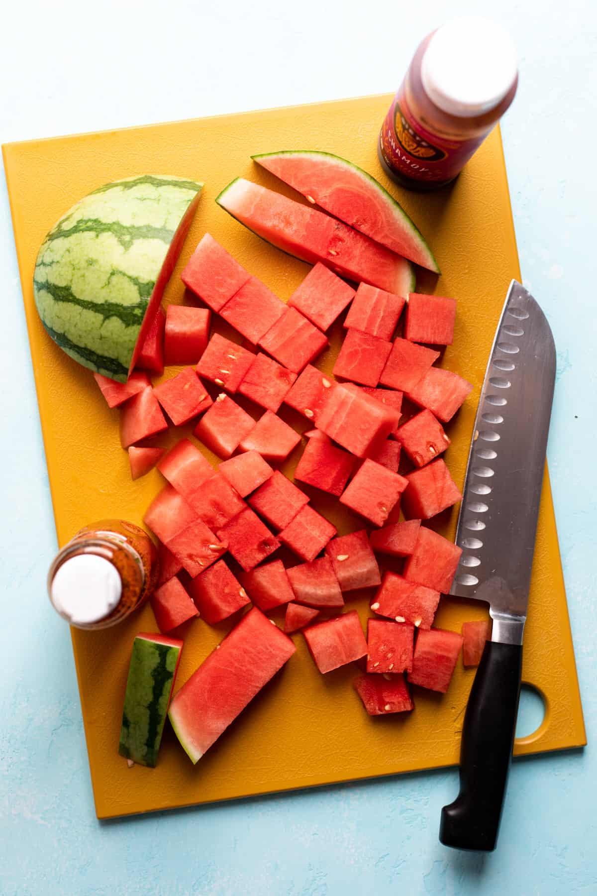 Cutting board with knife and watermelon being cubed.