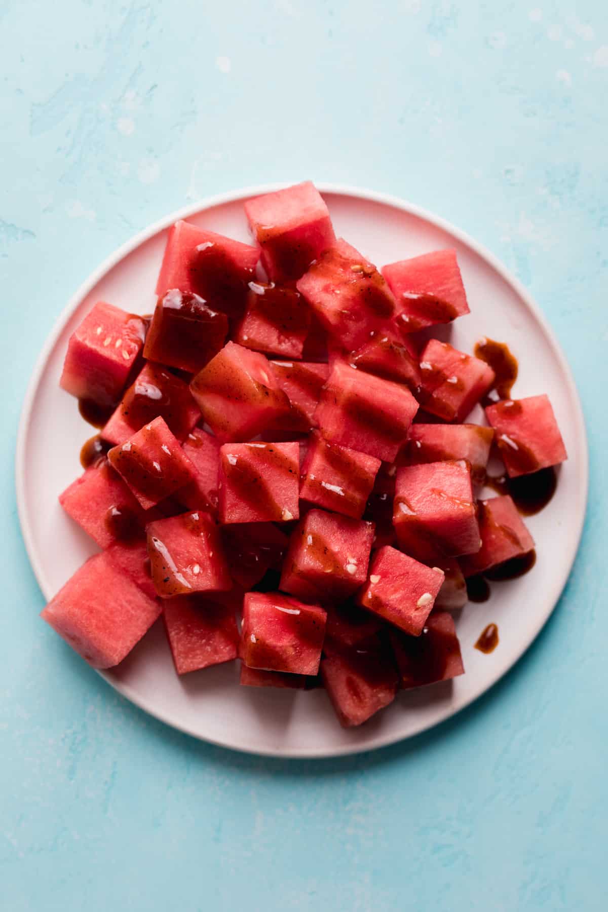 White plate with cubed watermelon drizzled with chamoy.