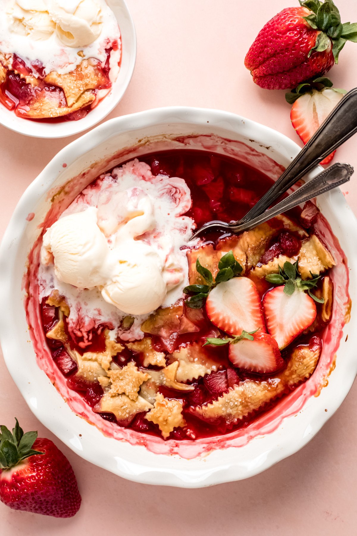 Strawberry cobbler being served with spoons and topped with vanilla ice cream. 