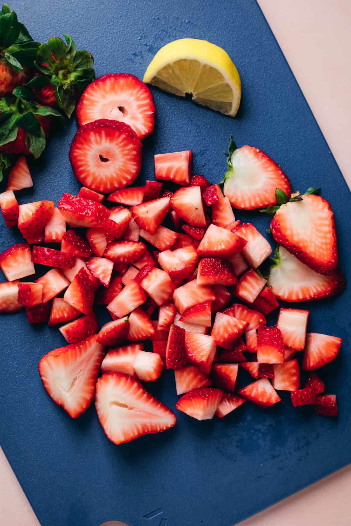Strawberries being sliced into bite size pieces on a blue cutting board.