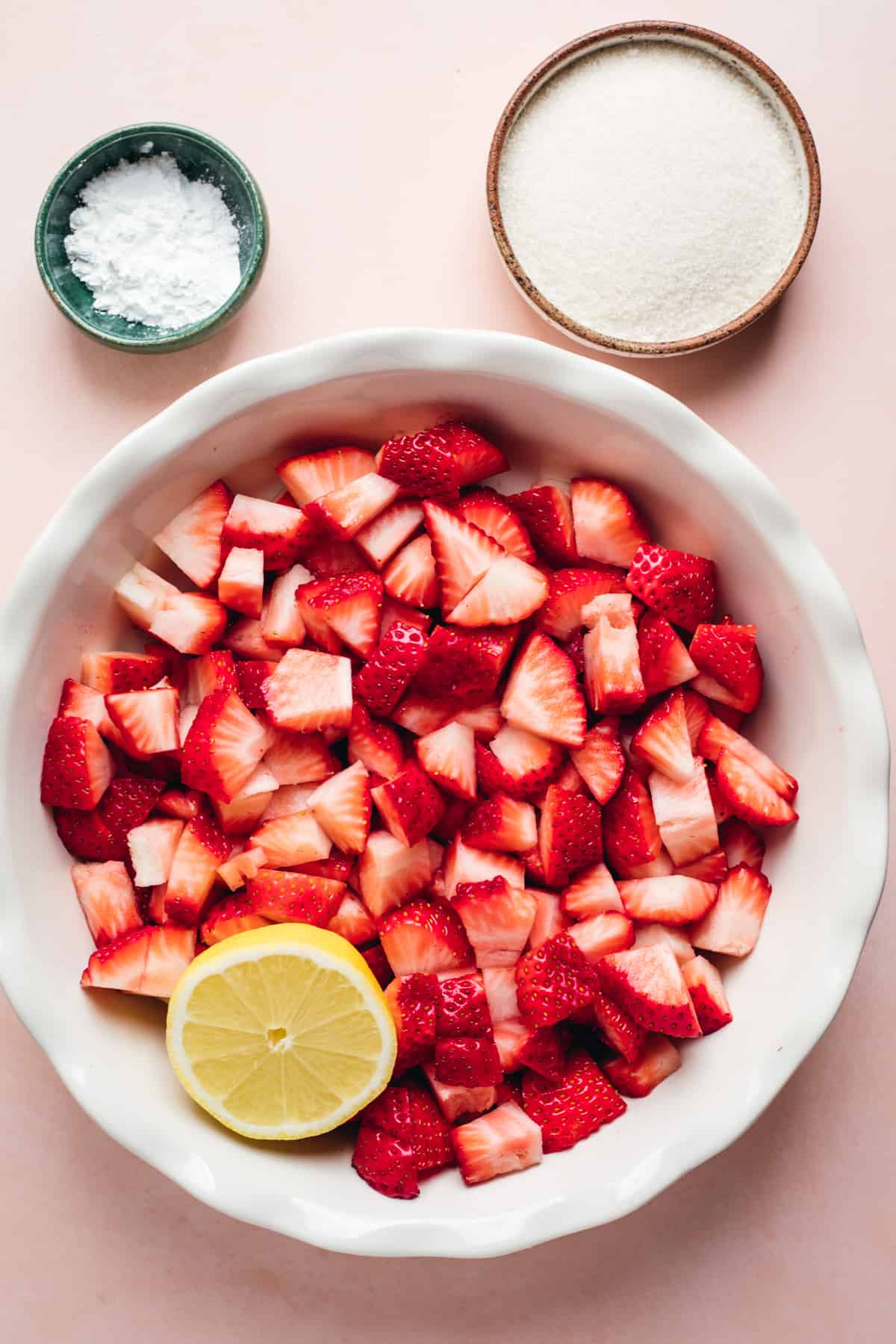 Chopped strawberries in a pie dish with a lemon, small bowls of cornstarch and sugar on the side.