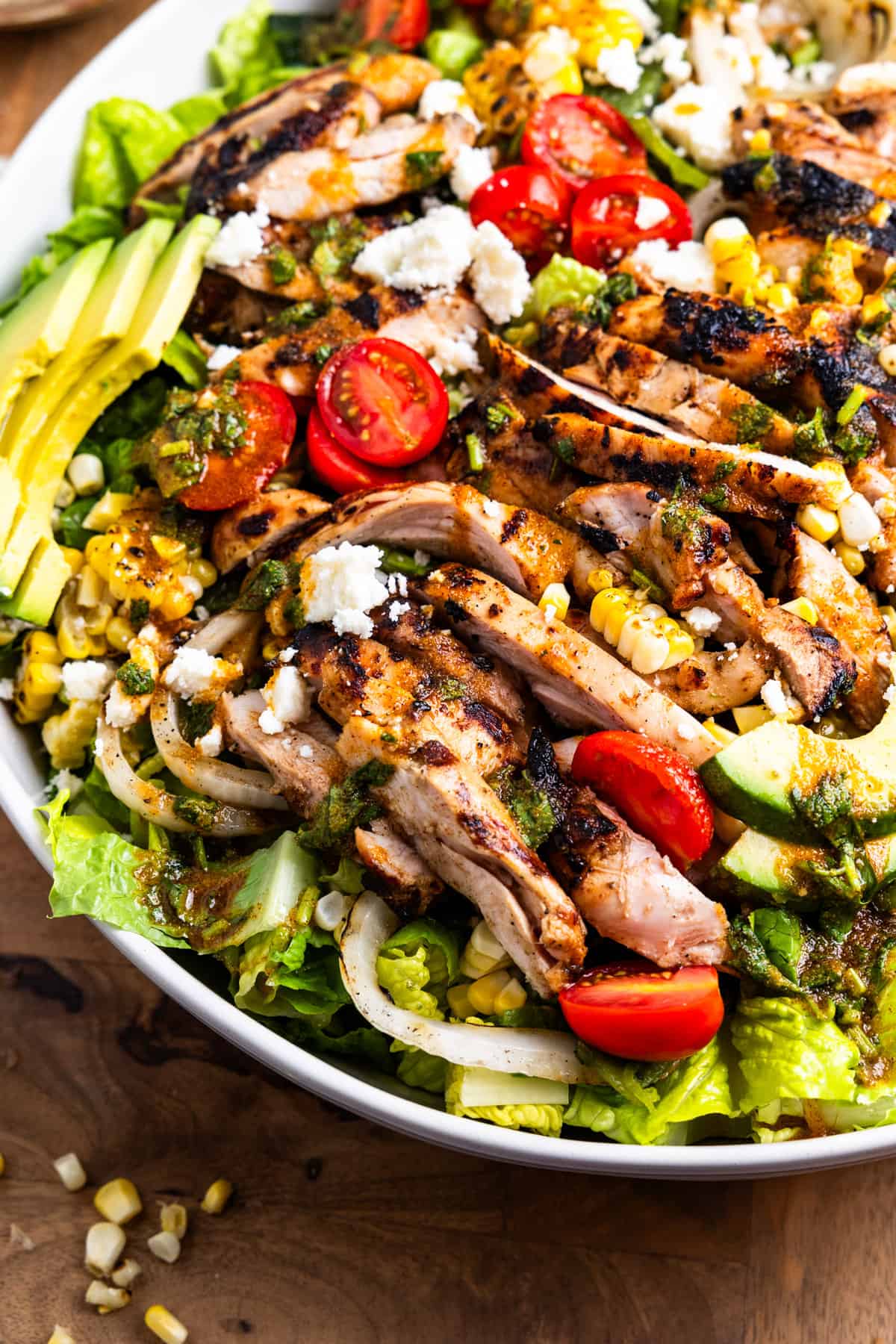 Bowl of sliced grilled chicken and fresh and grilled vegetables over lettuce for a salad.
