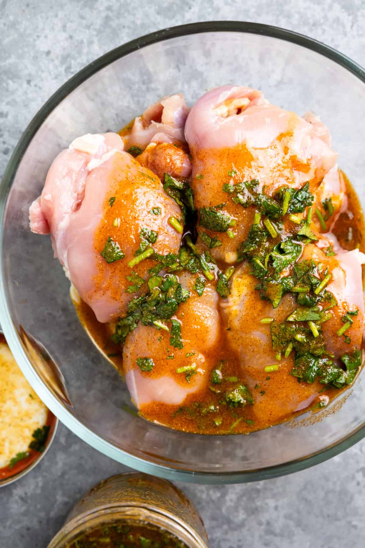 Marinade poured over the top of boneless, skinless chicken thighs in a glass bowl.