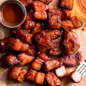 Pork belly burnt ends served with a cup of bbq sauce and a beer on the side.