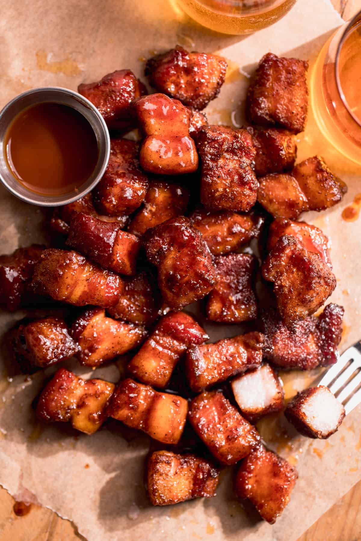 Pork belly burnt ends served with a cup of bbq sauce and a beer on the side. 