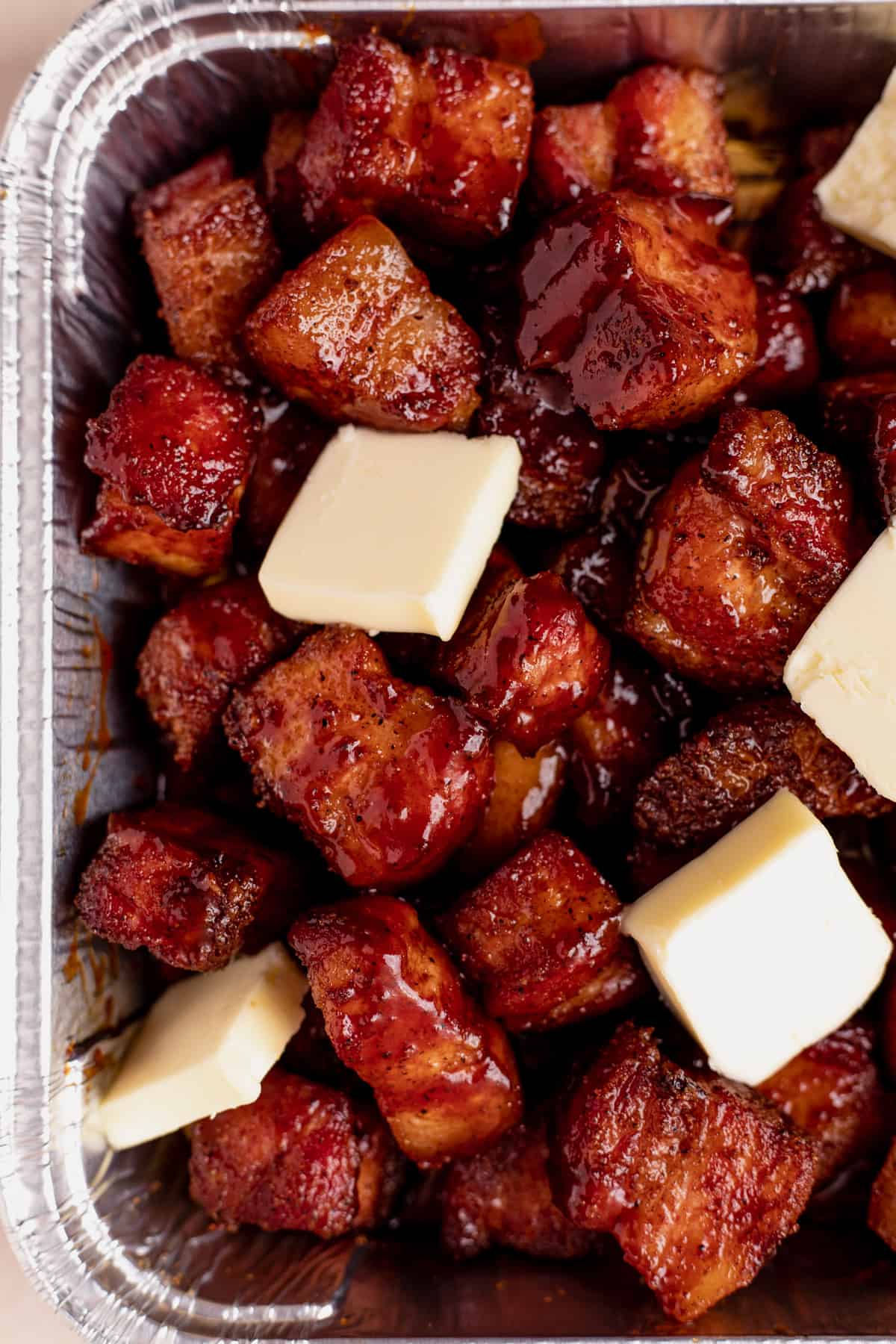 Slabs of butter on top of pork belly in an aluminum baking tin. 