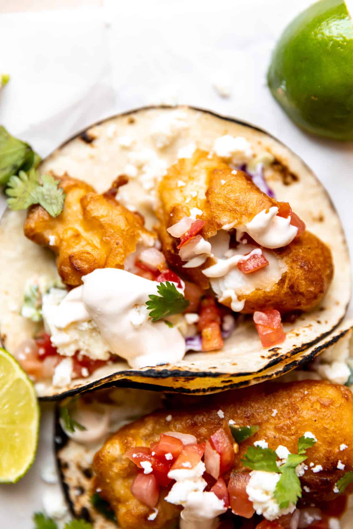 Up close view of fried fish on a charred corn tortilla topped with creamy sauce and Pico de Gallo. 