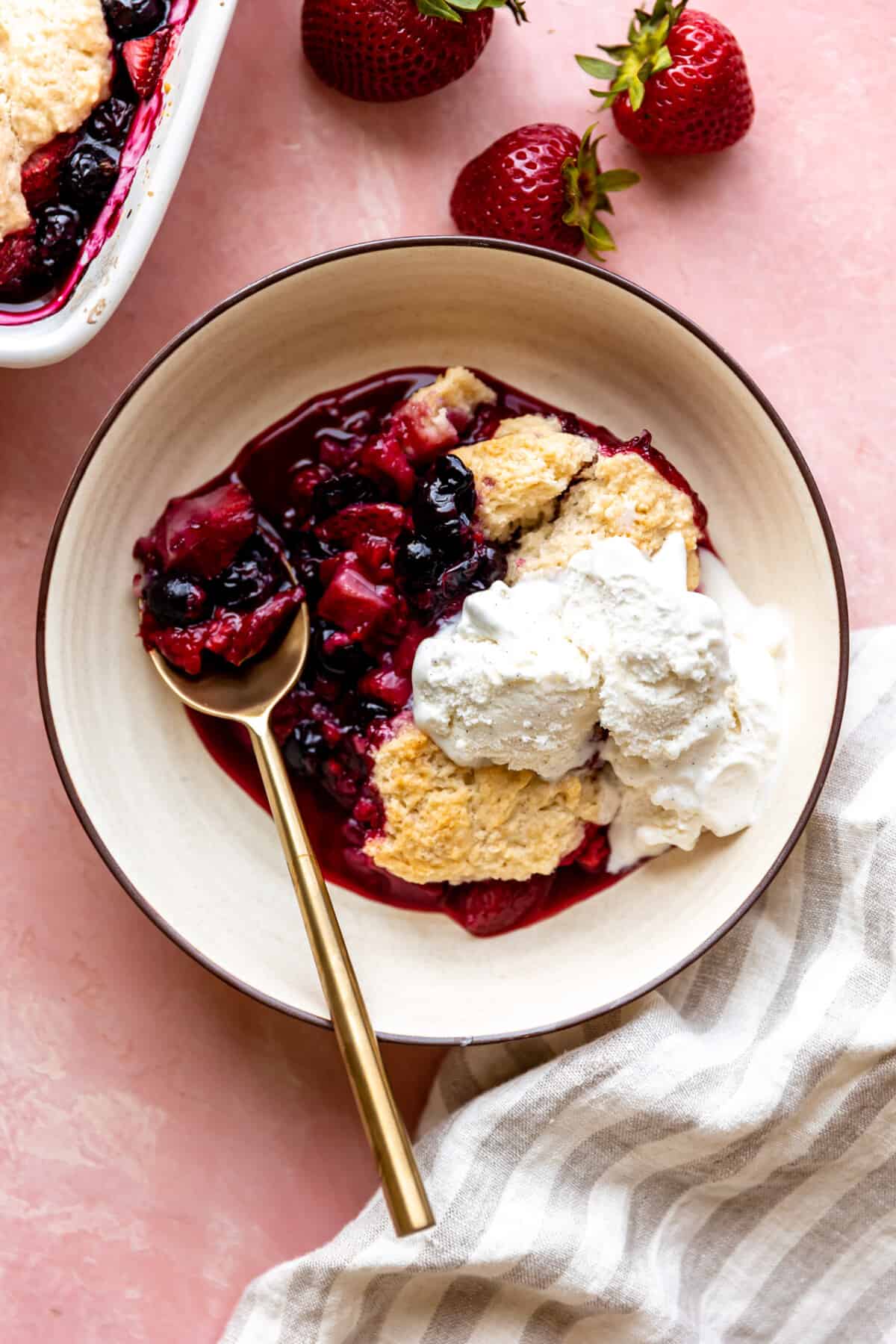Mixed berry cobbler served in a bowl with ice cream, spoon on the side.