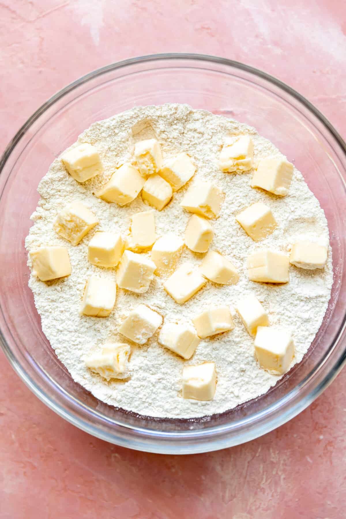 Glass bowl of flour and other dry ingredients for cobbler topping with cubes of cold butter on top. 