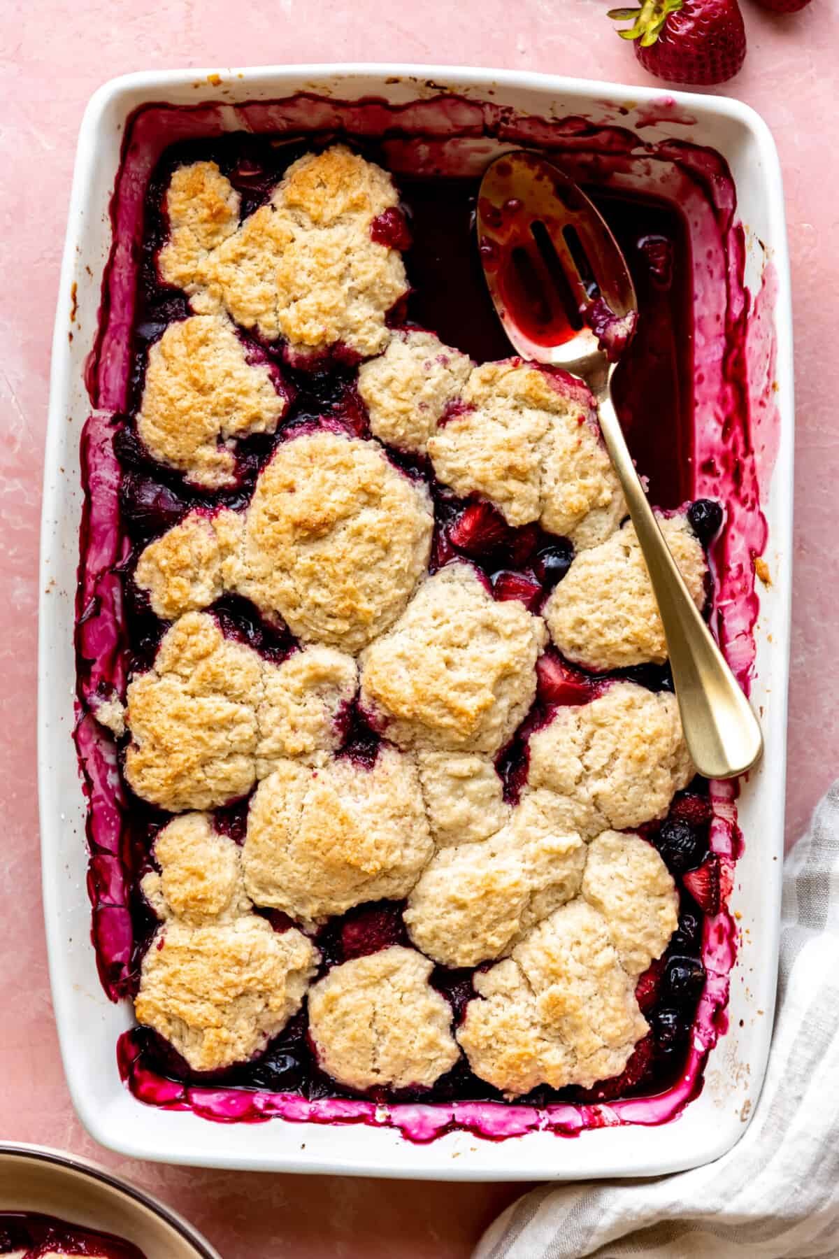 Baked mixed berry cobbler being scooped up with a spoon for serving. 