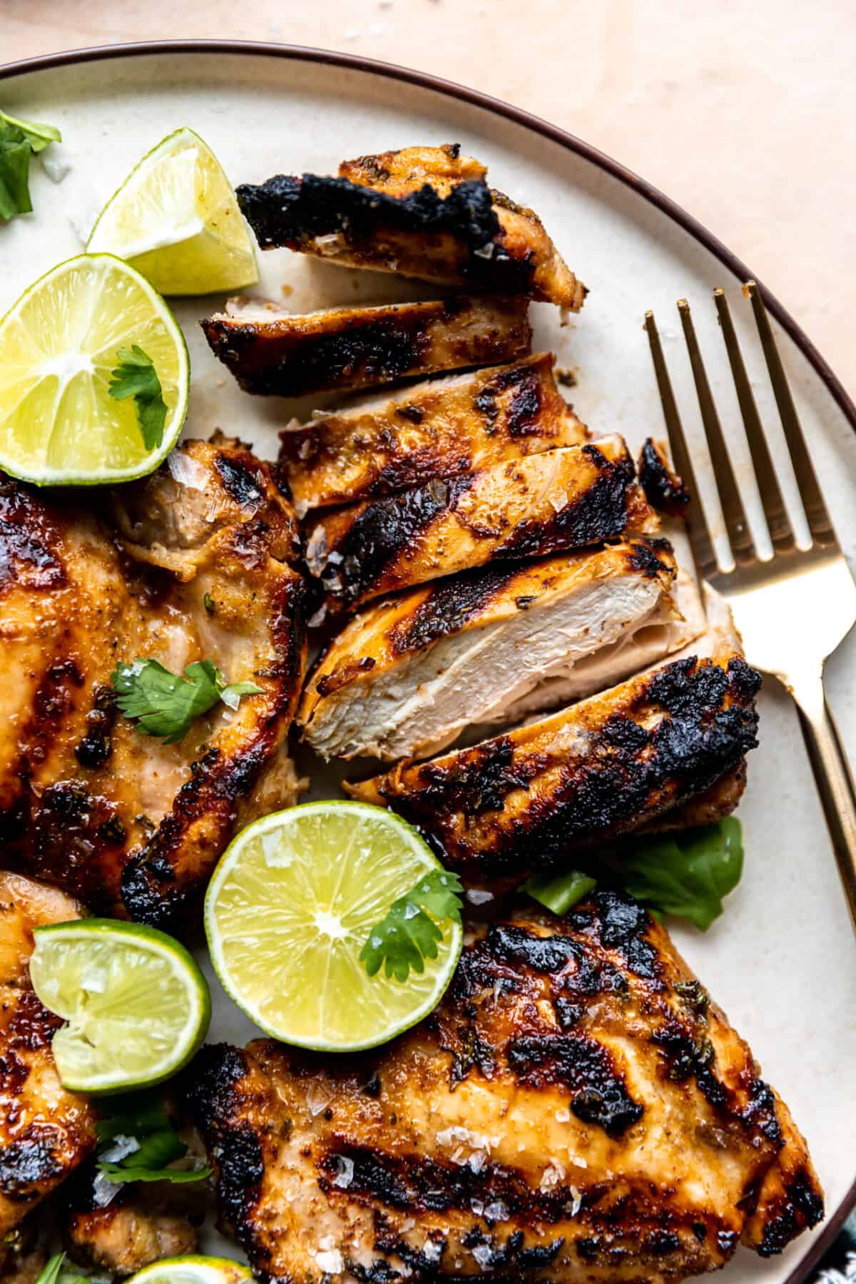 Grilled chicken thighs on a plate with lime wedges sliced with a fork on the side. 