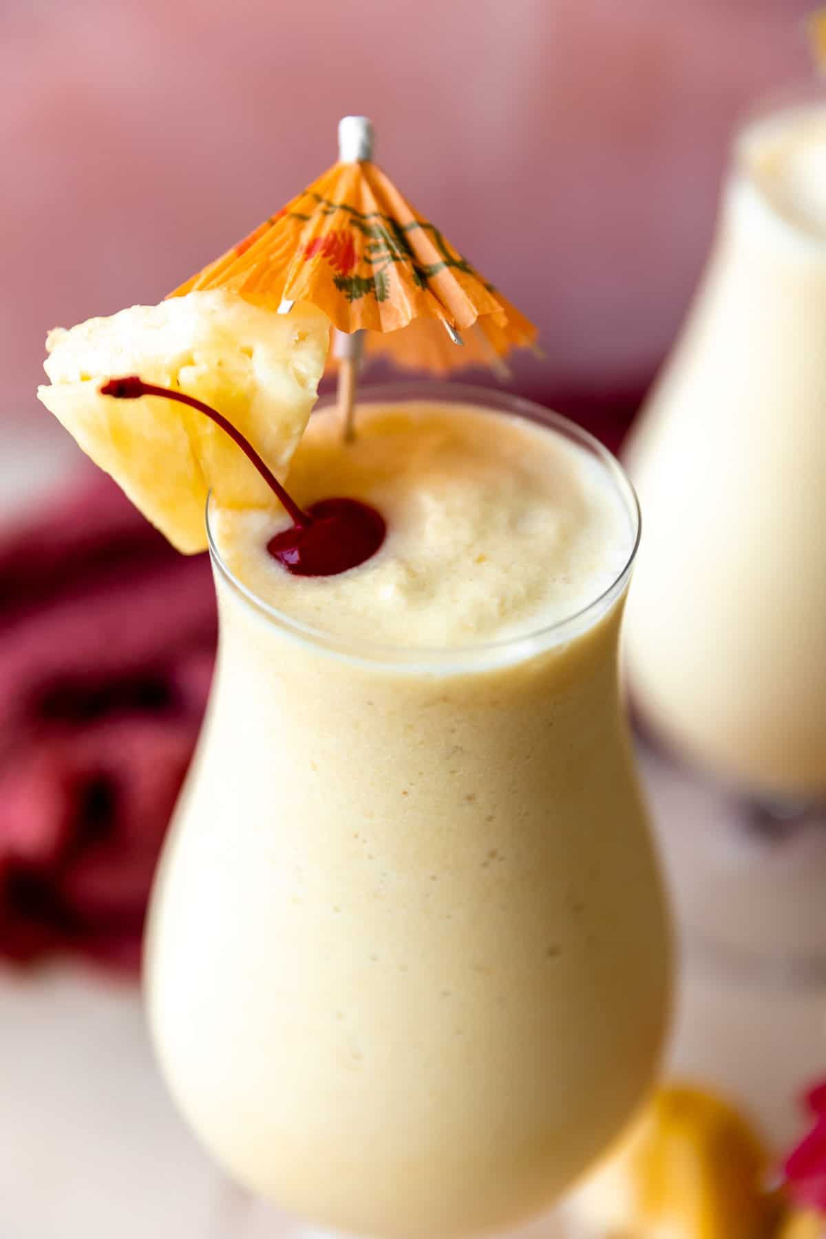 Glass filled with blended, frozen pina colada topped with cherries and a pineapple wedge. 