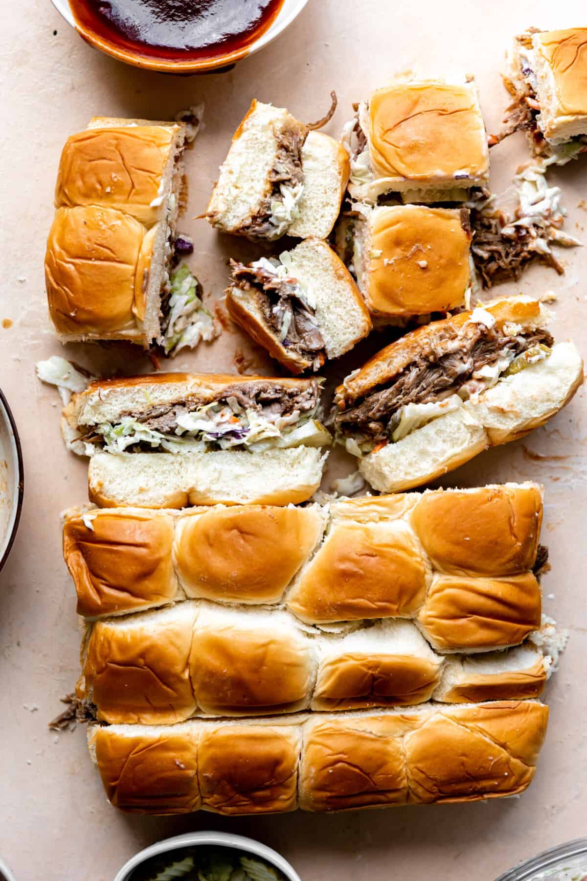 Hawaiian rolls with pulled pork, bbq sauce, coleslaw and pickles being cut apart. 