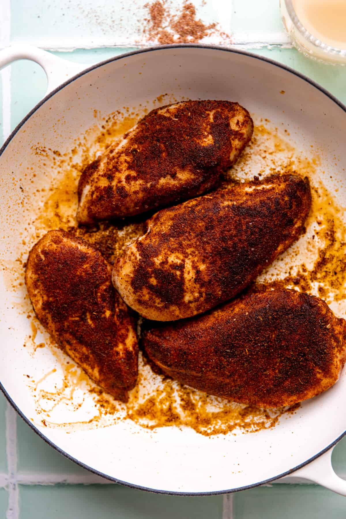 Chicken coated with a deep red colored homemade taco seasoning being seared in a skillet. 