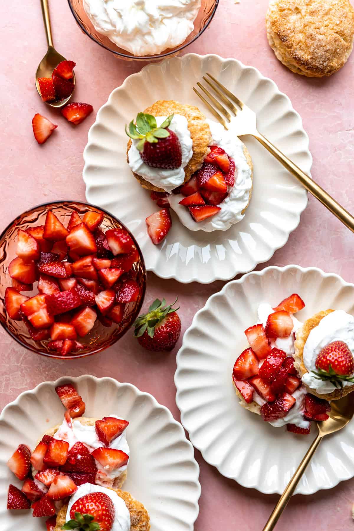Overhead shot of plates of strawberry shortcake served with a bowl of sliced strawberries and a bowl of whipped cream.