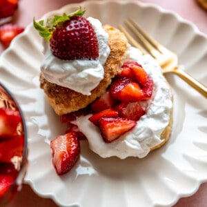 Strawberry shortcake served on a white scalloped plate, gold fork on the side.