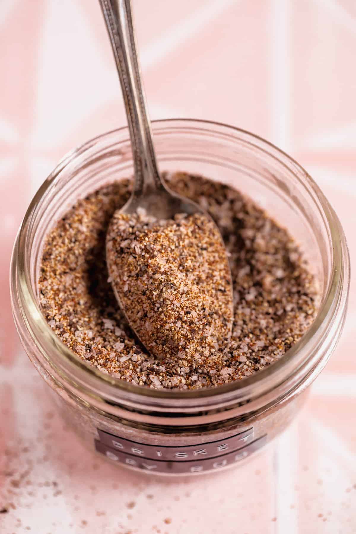 Spoon scooping up brisket rub from a glass jar.