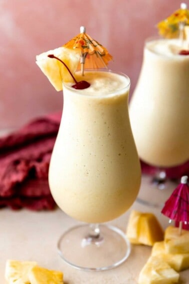 Glasses filled with smooth and creamy frozen pina colada topped with dark red cherries and wedges of pineapple.