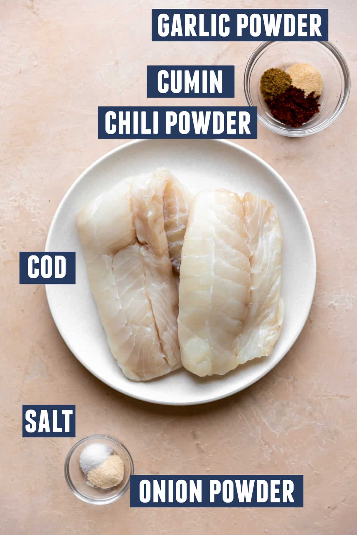 Ingredients needed to make grilled fish laid on the counter, cod on a white plate and two small bowls with salt and other seasonings. 