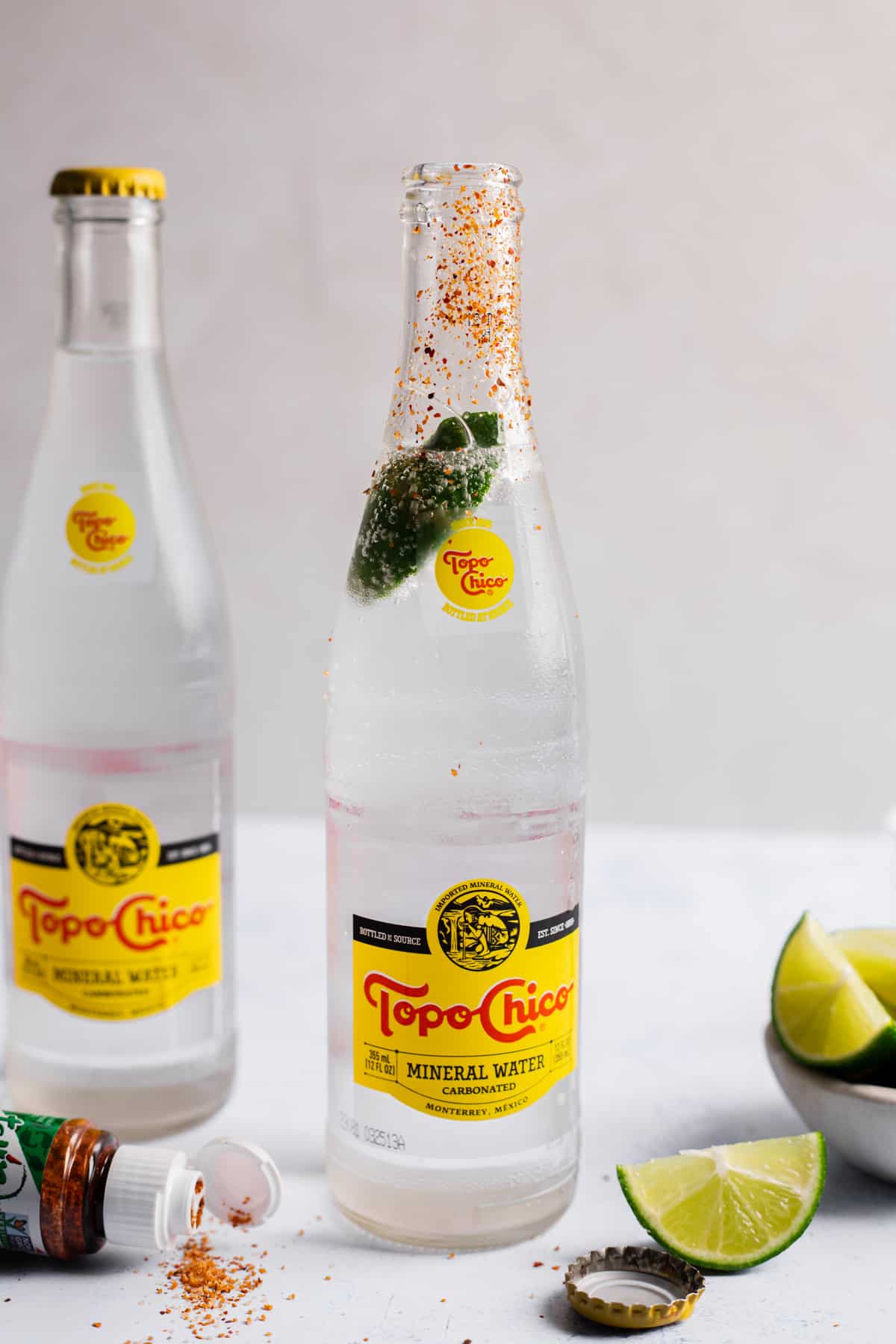 Bottle of Topo Chico with a tajin rim and lime wedge inside for a ranch water cocktail. 