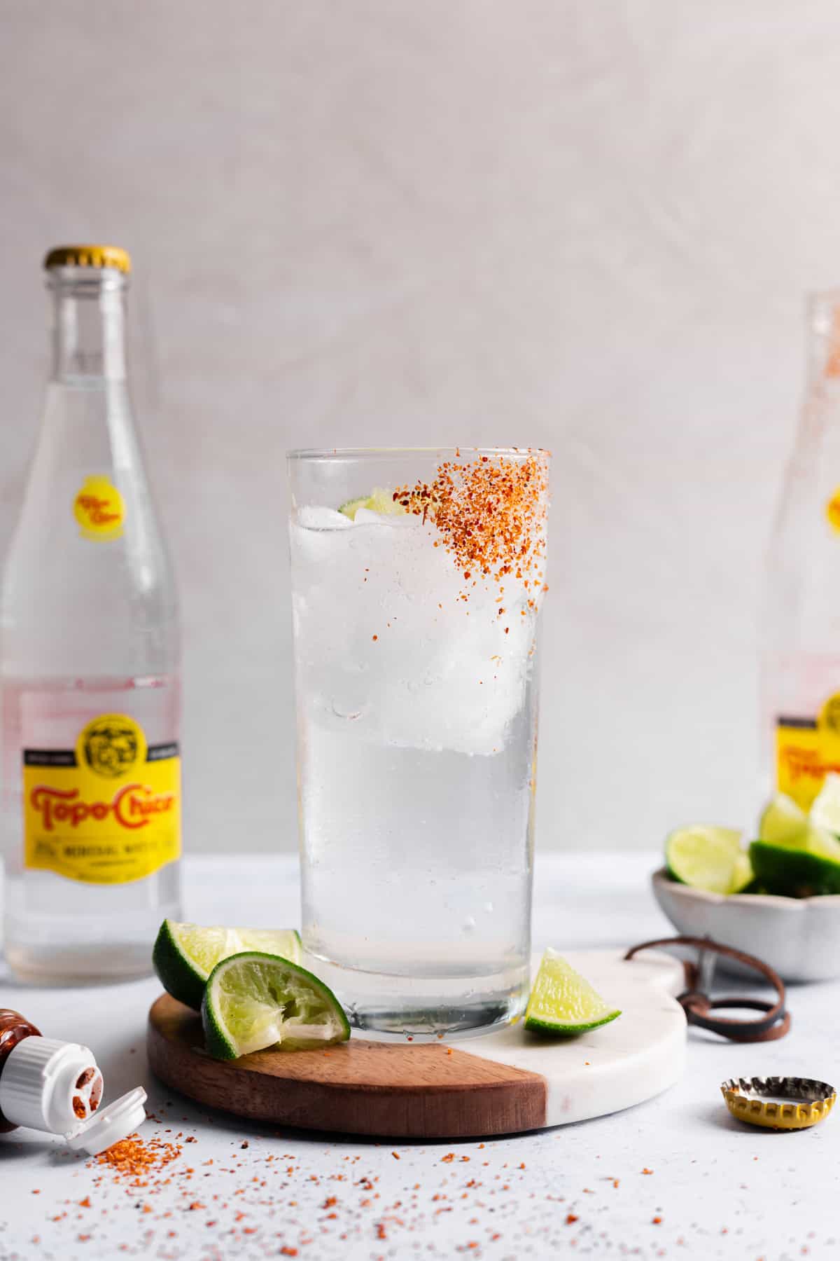A glass cup with tajin on the side and ice with clear liquid and a lime wedge inside.