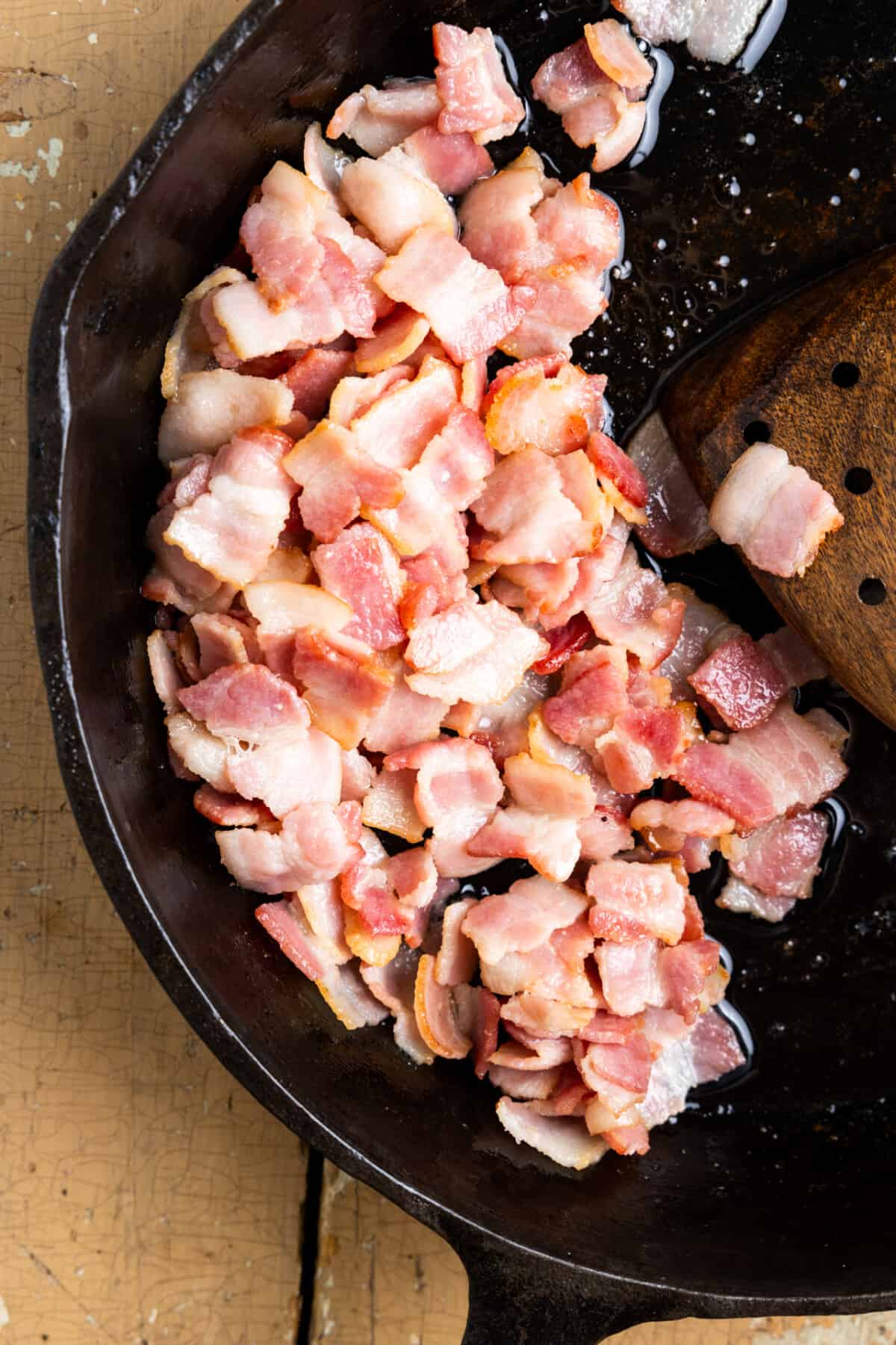 Bacon being cooked to render fat in a skillet.