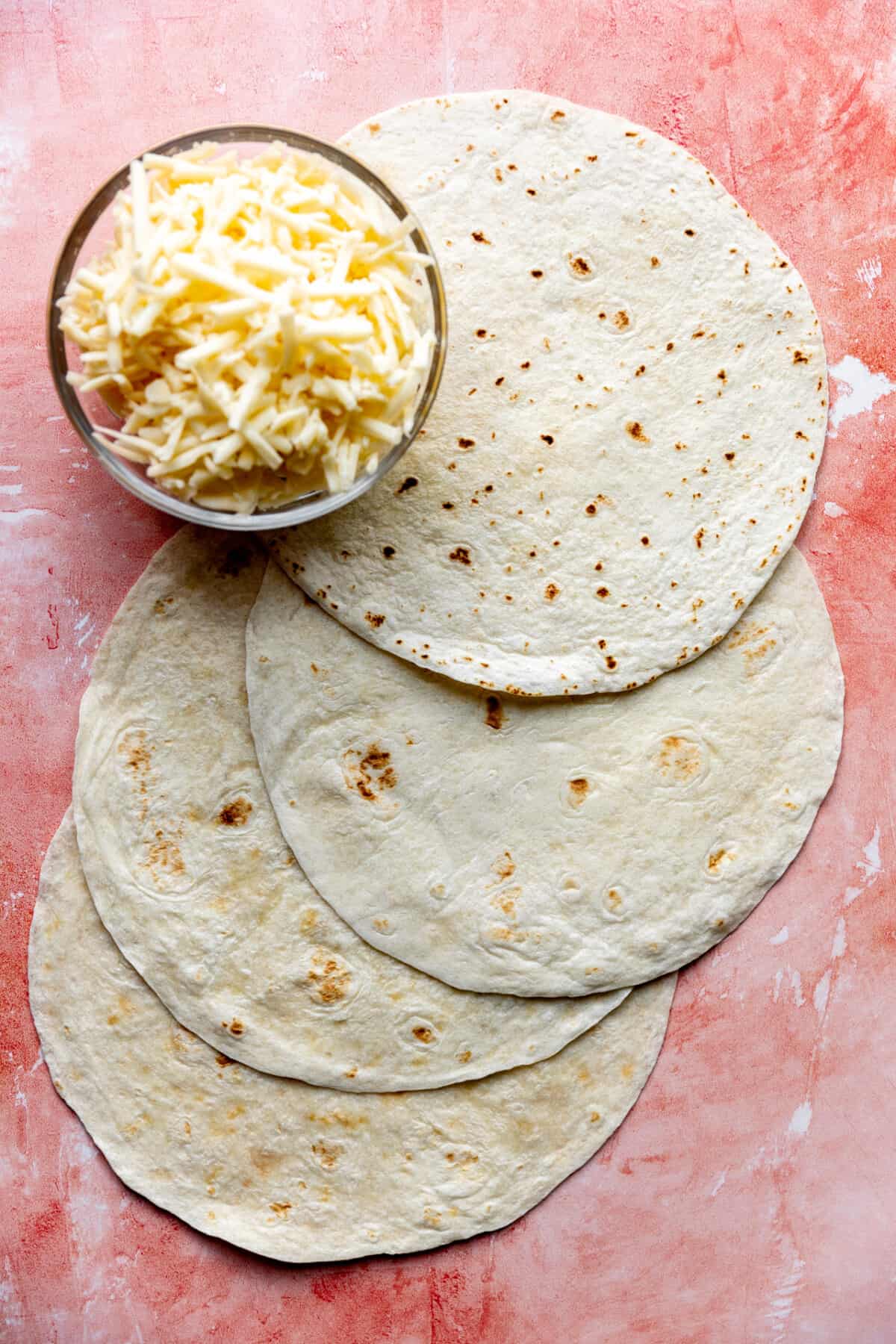 Stack of flour tortillas and a bowl of shredded cheese to make quesadillas. 