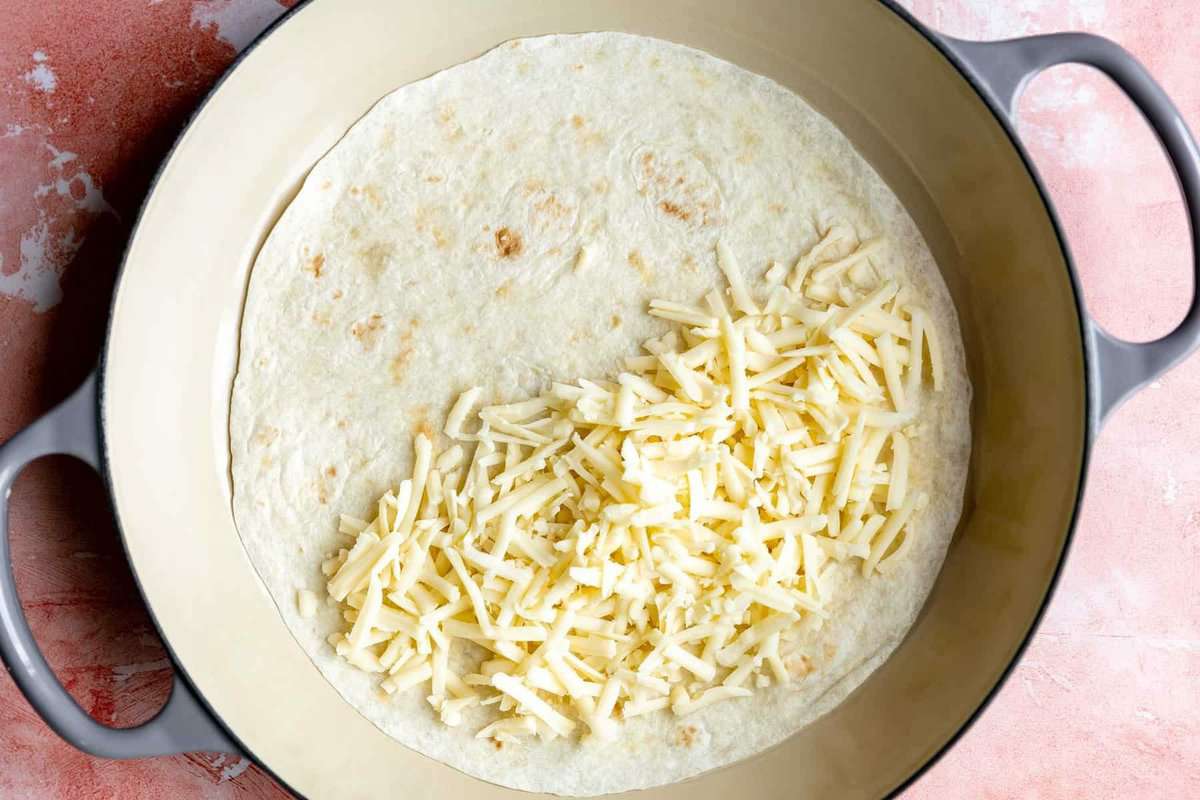 Skillet with a flour tortilla with shredded cheese on half.