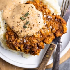 Chicken fried steak on a white plate with mashed potatoes and cream gravy on top.
