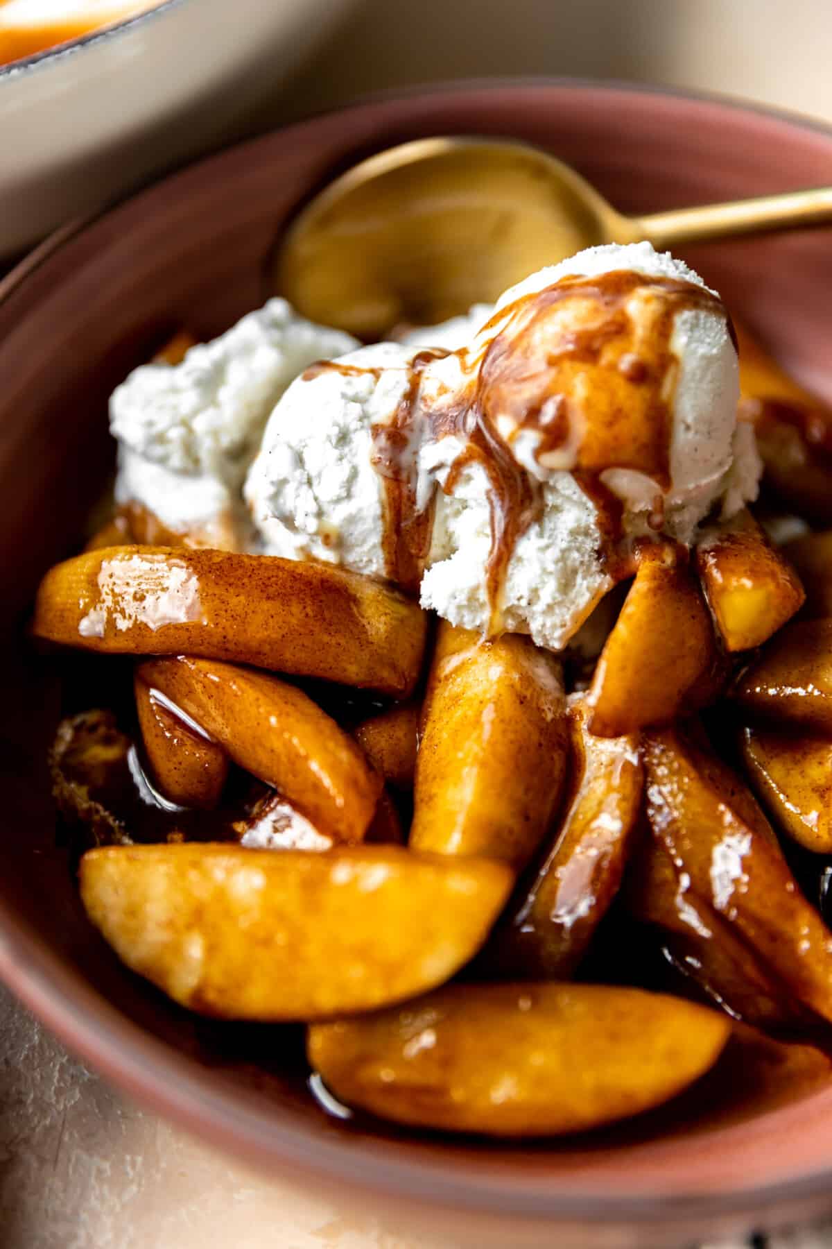 Up close view of fried apples topped with melting vanilla ice cream drizzled with cinnamon syrup. 