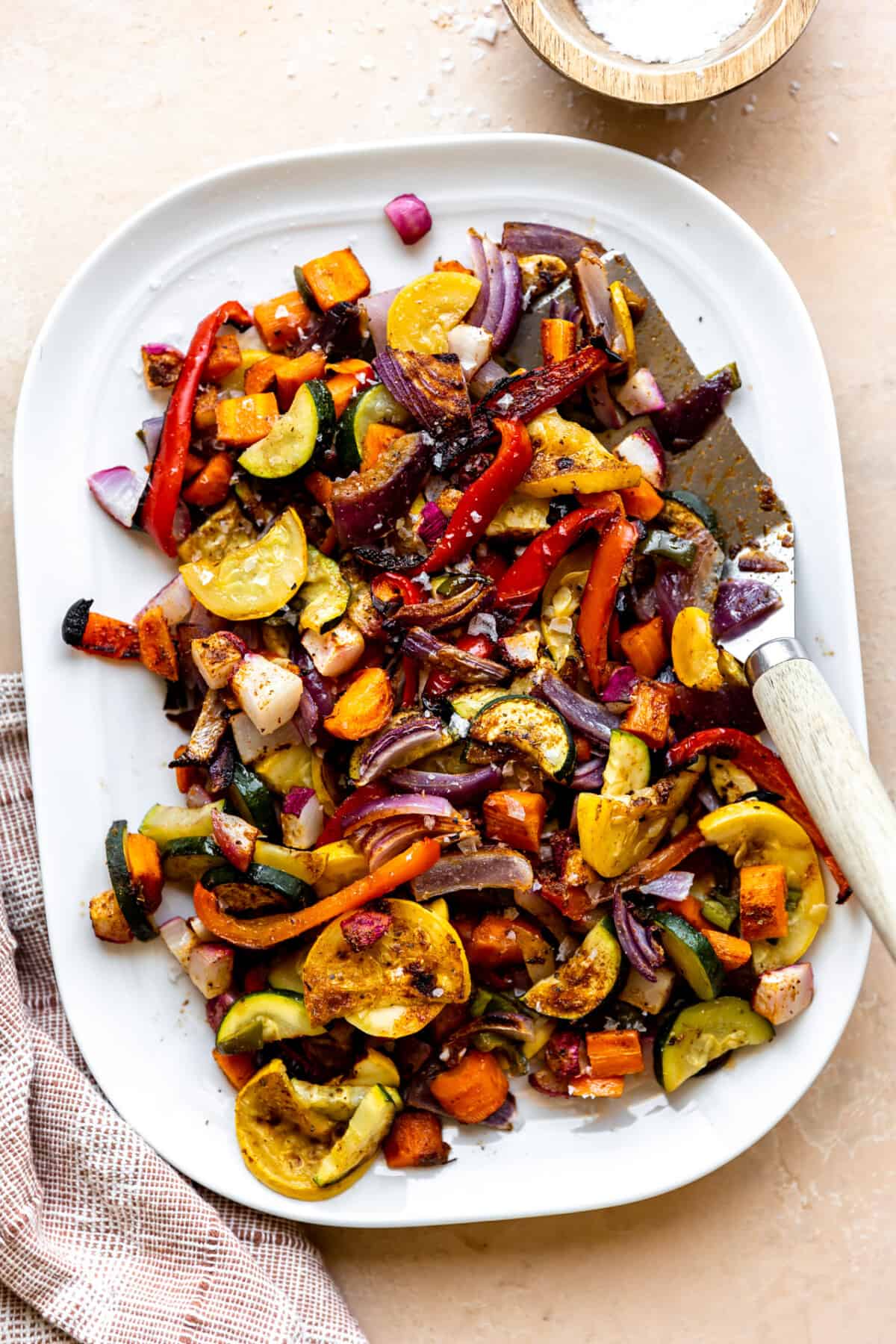 White plate filled with roasted mexican vegetables with a spatula for serving. 