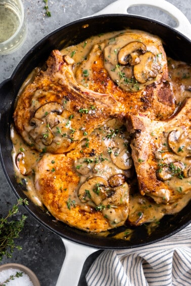 Skillet with pork chops in a cream of mushroom sauce topped with fresh herbs.