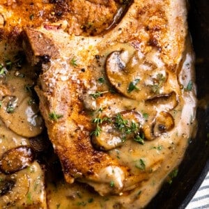 Up close of a pork chop with cream of mushroom soup garnished with parsley.