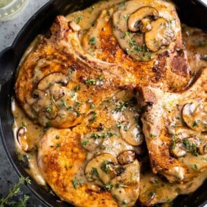 Skillet with pork chops in a cream of mushroom sauce topped with fresh herbs.